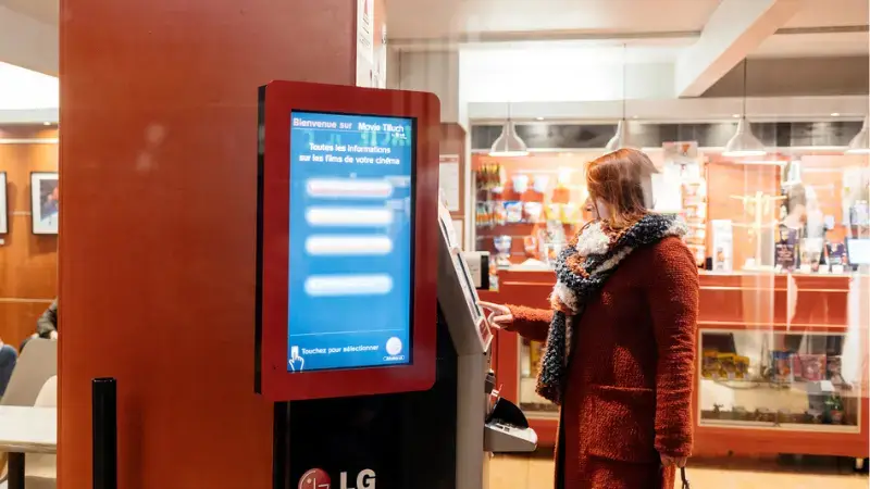 a woman buying a movie ticket through a movie theater kiosk inside a cinema building