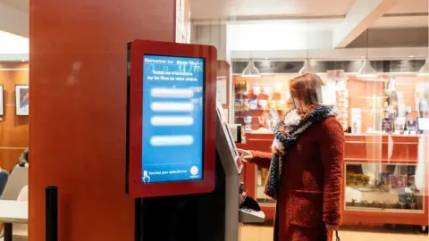 a woman buying a movie ticket through a movie theater kiosk inside a cinema building