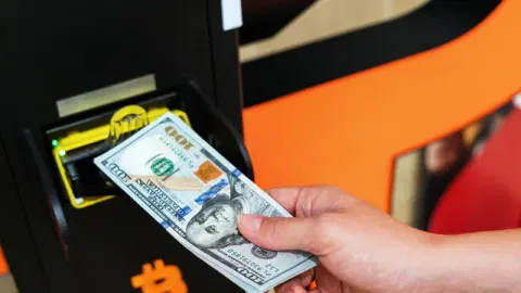 an individual inserting dollar bills into a kiosk
